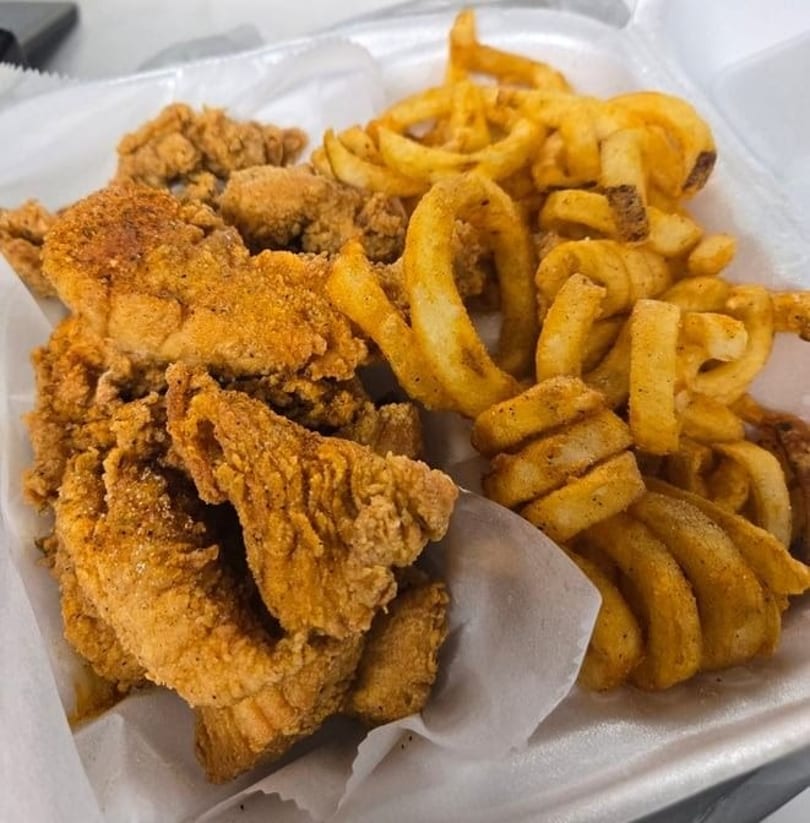 Crispy fried chicken tenders and seasoned curly fries in a white takeout container.