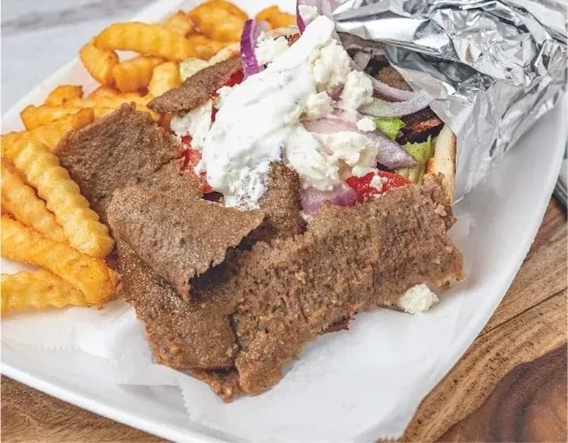 A gyro with meat, vegetables, and sauce, served with crinkle-cut fries on a white plate.