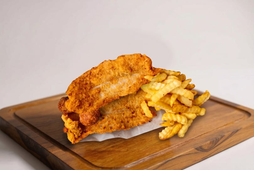 Golden-brown fried fish fillets and crinkle-cut fries served on a wooden board.
